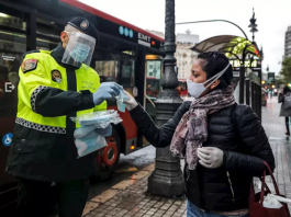 Un policía local entrega una mascarilla a una mujer en el centro de Valencia. / FOTO: Rober Solsona - Europa Press.