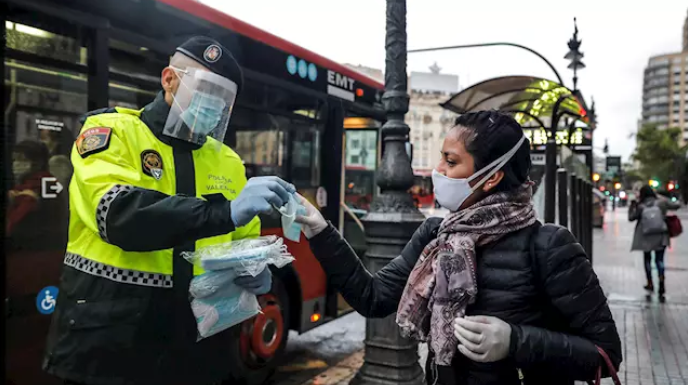 El Govern posa data a la fi de les mascaretes en el transport públic Un policía local entrega una mascarilla a una mujer en el centro de Valencia. / FOTO: Rober Solsona - Europa Press.