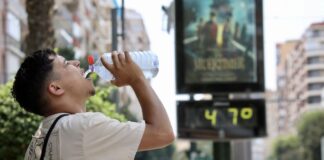 Un hombre hidratándose frente a un termómetro de calle que muestra la ola de calor