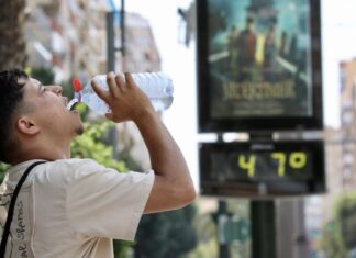 Un hombre hidratándose frente a un termómetro de calle que muestra la ola de calor