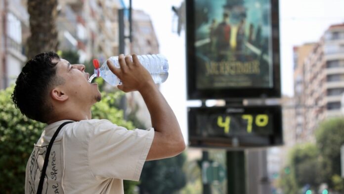 7televalencia ola de calor eb valencia Un hombre hidratándose frente a un termómetro de calle que muestra la ola de calor