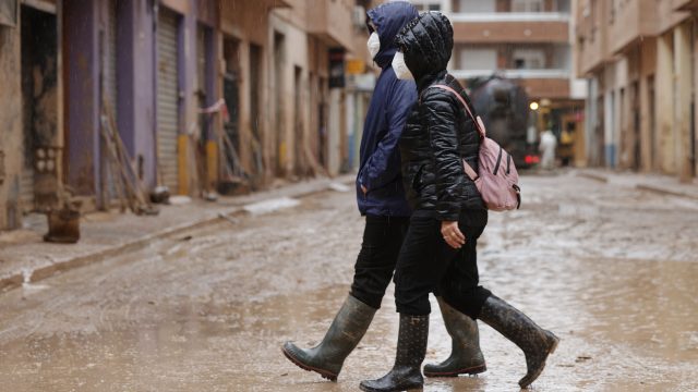 Dos personas caminan protegidas con mascarillas y botas de agua por las calles de Catarroja. / MANUEL BRUQUE (EFE)