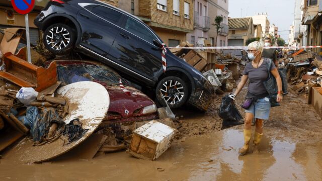 Los vecinos limpian las calles junto a varios coches apilados en Catarroja. / CHEMA MOYA (EFE) La nueva ayuda "sin burocracia ni impuestos" de hasta 2.500 euros por la DANA: requisitos y cómo solicitarla